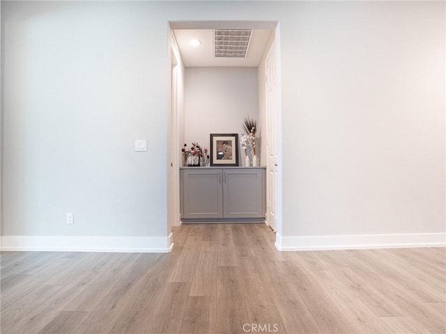 hall with baseboards, visible vents, and light wood-type flooring