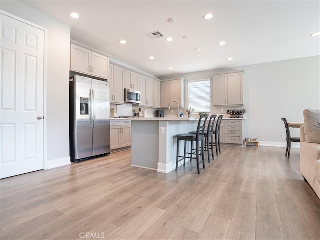 kitchen featuring light wood finished floors, stainless steel appliances, light countertops, visible vents, and a kitchen bar