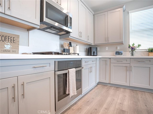 kitchen featuring light countertops, light wood-style floors, stainless steel appliances, and gray cabinetry