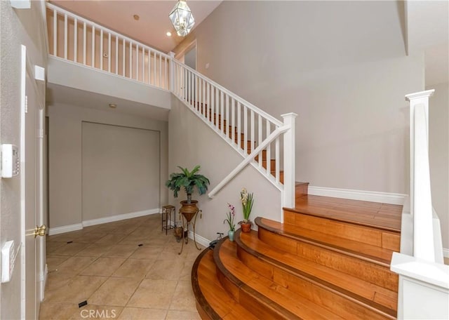 staircase with baseboards, tile patterned flooring, and a high ceiling
