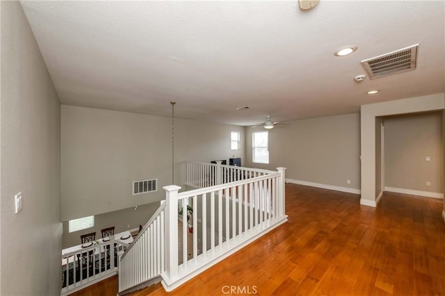 corridor with baseboards, wood finished floors, an upstairs landing, and visible vents