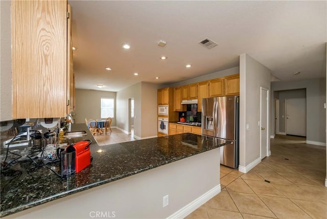 kitchen featuring dark stone counters, visible vents, baseboards, white appliances, and light tile patterned floors