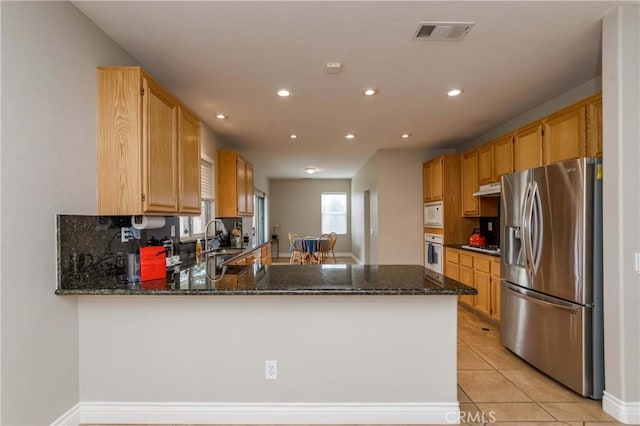 kitchen featuring under cabinet range hood, stainless steel appliances, dark stone countertops, visible vents, and a peninsula