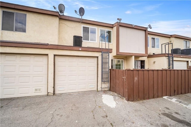 view of front of property with fence, driveway, stucco siding, central air condition unit, and an attached garage