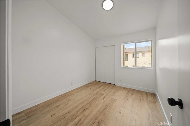 spare room featuring vaulted ceiling, light wood-type flooring, and baseboards