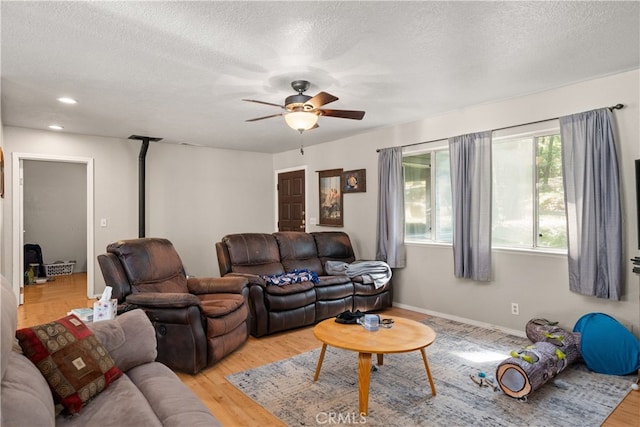 living area featuring a ceiling fan, a textured ceiling, light wood-style floors, a wood stove, and recessed lighting