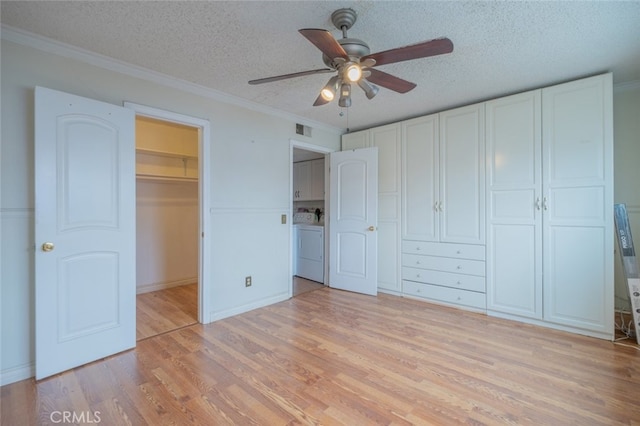 unfurnished bedroom featuring a textured ceiling, a spacious closet, light wood-style floors, a closet, and washer / clothes dryer