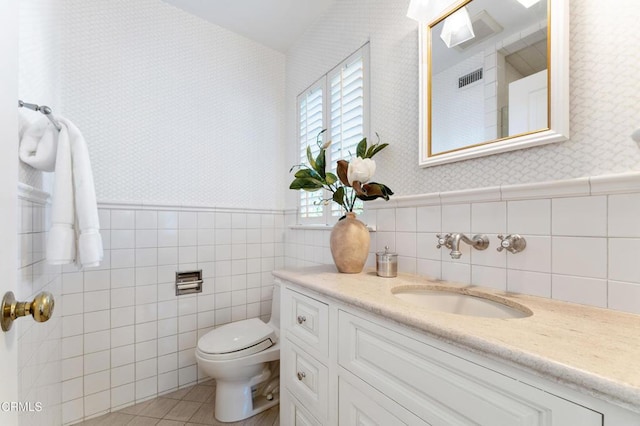 bathroom with toilet, wallpapered walls, wainscoting, and tile patterned floors