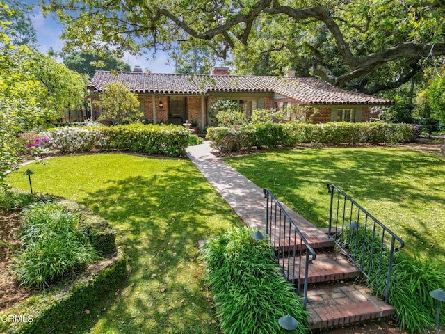 view of front of house with a chimney, a tiled roof, a front yard, and brick siding