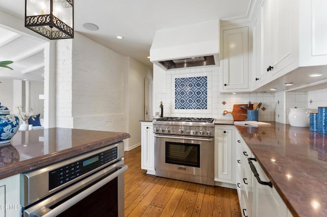 kitchen featuring tasteful backsplash, white cabinets, stainless steel appliances, light wood finished floors, and custom exhaust hood