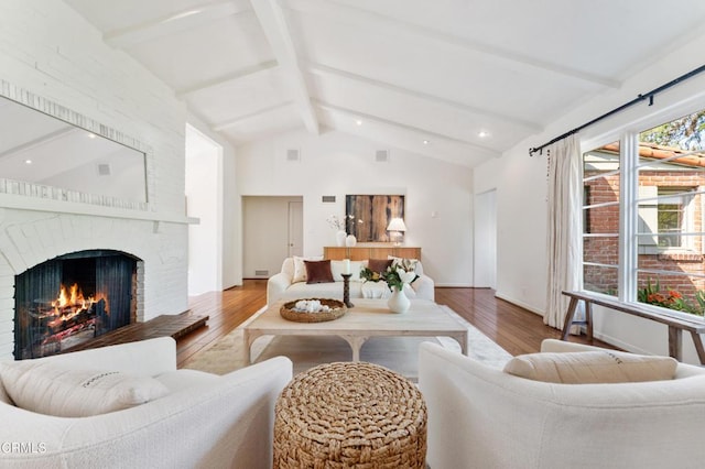 living room with a brick fireplace, visible vents, vaulted ceiling with beams, and wood finished floors