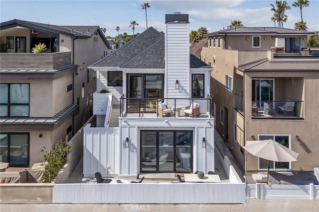 back of house featuring a chimney, a balcony, and fence
