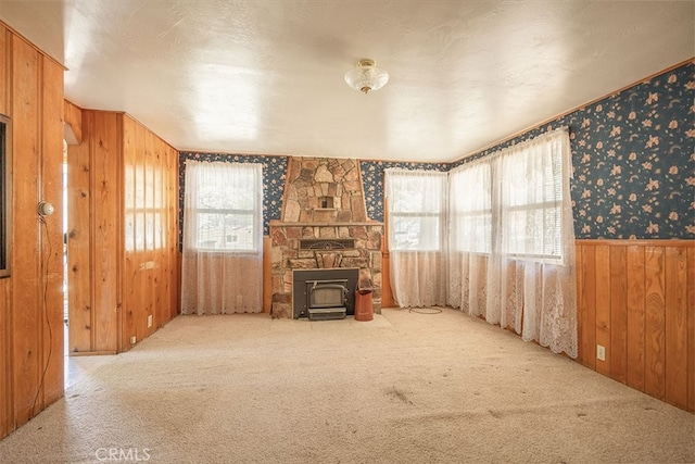 unfurnished living room featuring carpet flooring, wood walls, a wood stove, and wallpapered walls