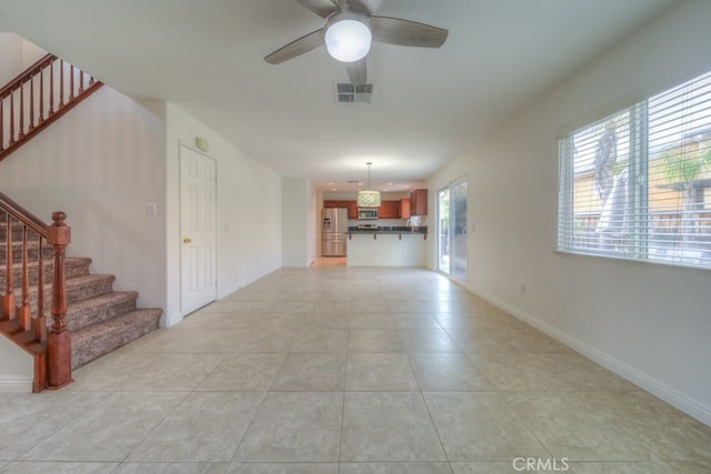 unfurnished living room with stairway, a ceiling fan, light tile patterned flooring, baseboards, and visible vents