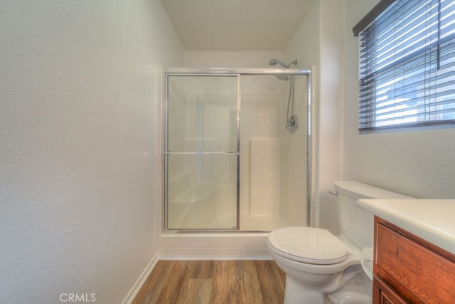 bathroom featuring a shower stall, toilet, wood finished floors, vanity, and baseboards