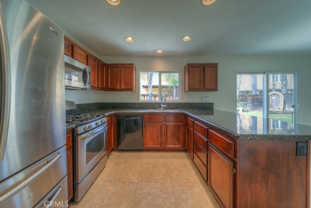 kitchen with light tile patterned floors, a sink, dark stone counters, a peninsula, and appliances with stainless steel finishes