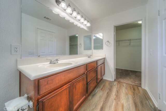 bathroom featuring wood finished floors, a sink, visible vents, and double vanity