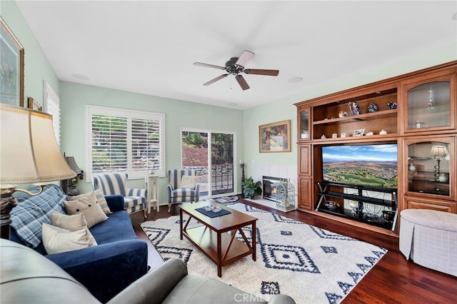 living room featuring ceiling fan, a tiled fireplace, and wood finished floors