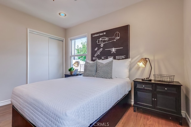 bedroom with wood finished floors, a closet, and baseboards