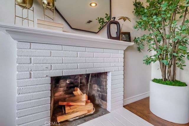 room details featuring baseboards, a brick fireplace, wood finished floors, and visible vents