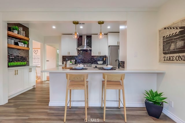 kitchen with wall chimney exhaust hood, tasteful backsplash, freestanding refrigerator, wood finished floors, and a breakfast bar