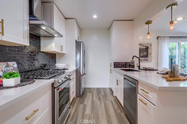 kitchen with a peninsula, a sink, light wood-type flooring, wall chimney range hood, and appliances with stainless steel finishes