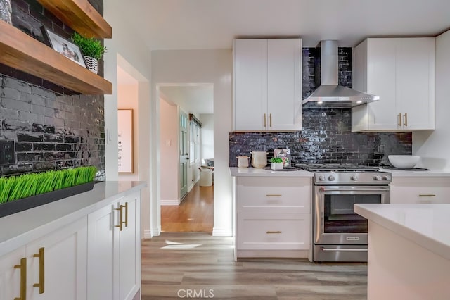 kitchen with wall chimney exhaust hood, light countertops, light wood-type flooring, and gas range