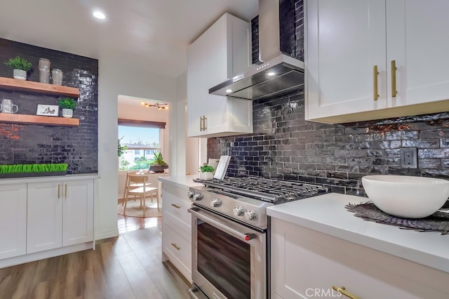 kitchen featuring light wood finished floors, backsplash, wall chimney range hood, stainless steel stove, and white cabinetry