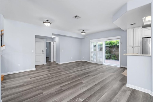 unfurnished living room featuring baseboards, wood finished floors, and visible vents
