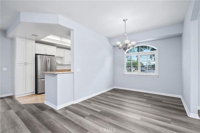 unfurnished dining area featuring baseboards, a notable chandelier, and wood finished floors