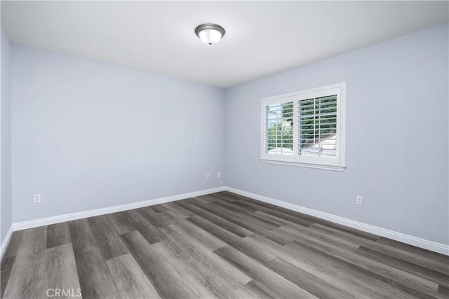spare room with baseboards and dark wood-type flooring