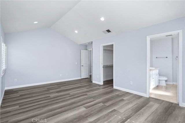 unfurnished bedroom with visible vents, baseboards, wood finished floors, lofted ceiling, and a spacious closet