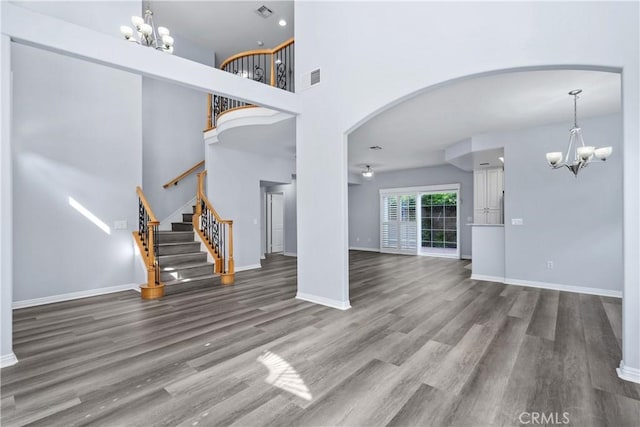 unfurnished living room with an inviting chandelier, arched walkways, wood finished floors, and visible vents