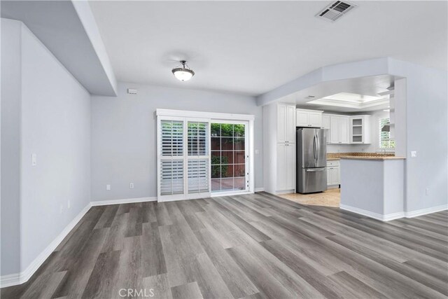 unfurnished living room with visible vents, baseboards, wood finished floors, and a tray ceiling