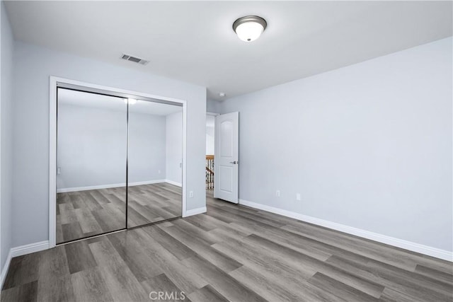 unfurnished bedroom featuring baseboards, visible vents, wood finished floors, and a closet