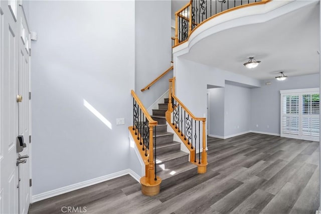 stairway featuring baseboards, wood finished floors, and a towering ceiling