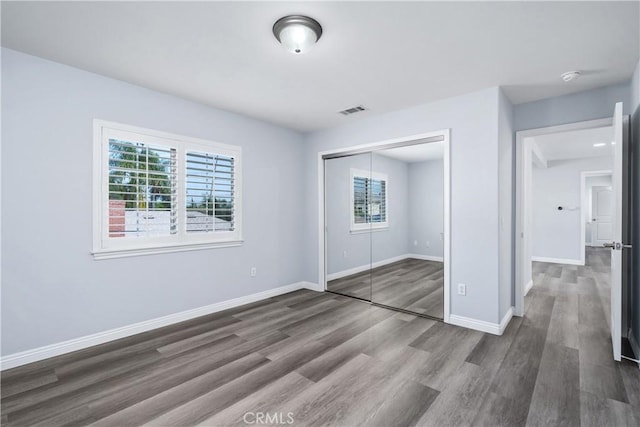 unfurnished bedroom with baseboards, a closet, dark wood finished floors, and visible vents