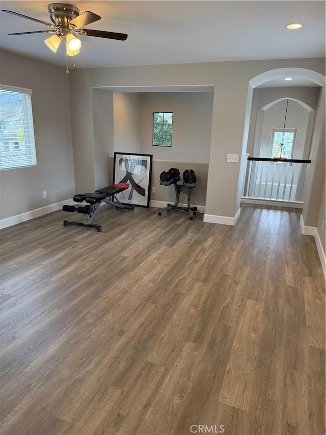 exercise room featuring recessed lighting, wood finished floors, a ceiling fan, arched walkways, and baseboards