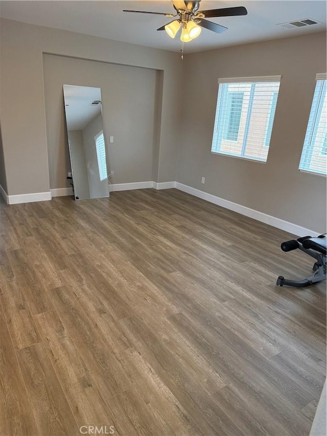 unfurnished room featuring wood finished floors, visible vents, a ceiling fan, and baseboards