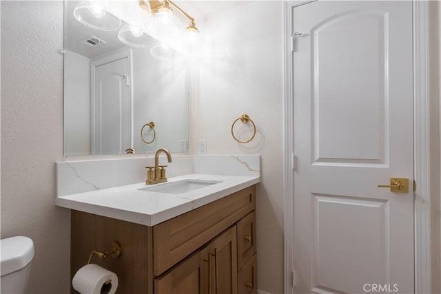 bathroom with toilet, a textured wall, vanity, and visible vents