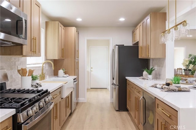kitchen with light brown cabinetry, a sink, light wood-style floors, decorative backsplash, and appliances with stainless steel finishes
