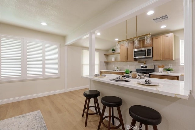 kitchen with a kitchen bar, decorative backsplash, appliances with stainless steel finishes, and visible vents