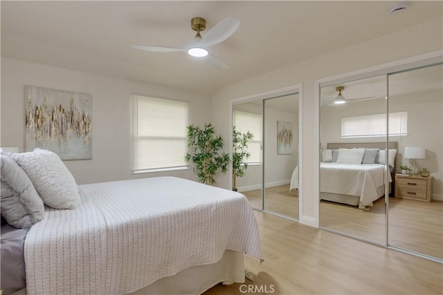 bedroom featuring baseboards, multiple windows, multiple closets, and light wood-style floors