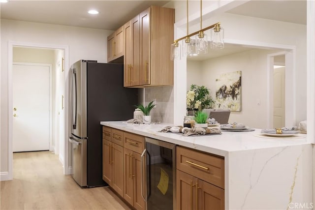 kitchen featuring beverage cooler, light wood finished floors, freestanding refrigerator, light stone countertops, and a peninsula