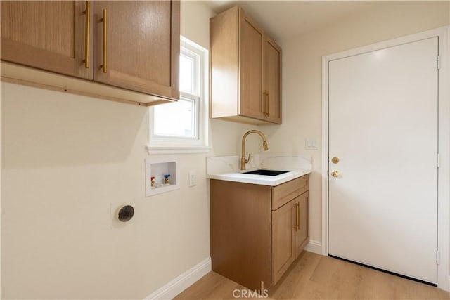 clothes washing area featuring a sink, baseboards, light wood-style floors, hookup for a washing machine, and cabinet space