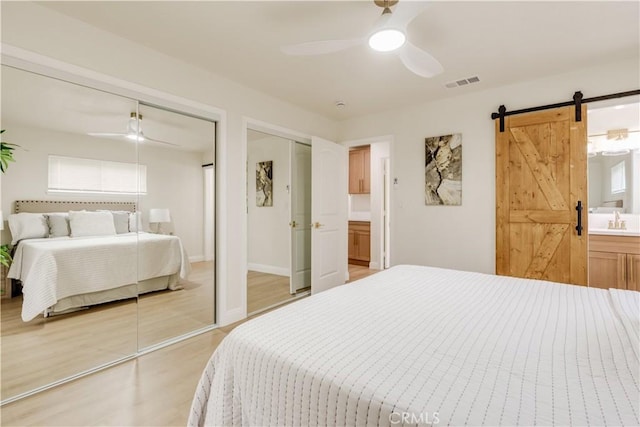 bedroom with a barn door, a sink, multiple closets, light wood finished floors, and visible vents