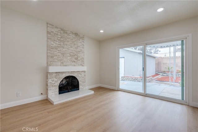 unfurnished living room with recessed lighting, wood finished floors, baseboards, and a stone fireplace