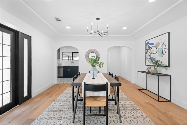 dining space featuring a chandelier, light wood-style floors, arched walkways, baseboards, and visible vents