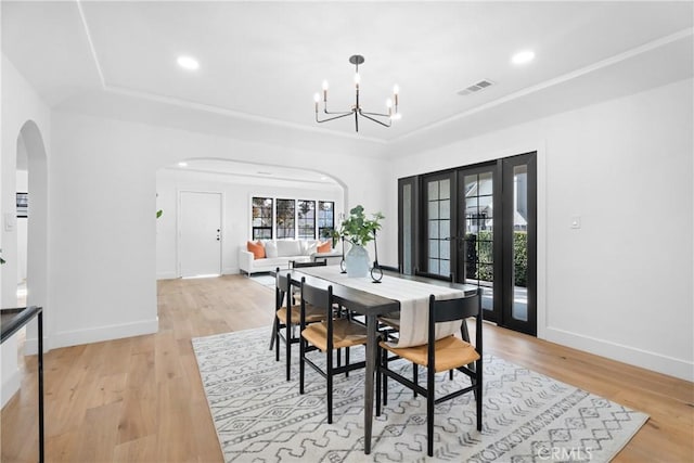dining space with baseboards, arched walkways, light wood-type flooring, and an inviting chandelier