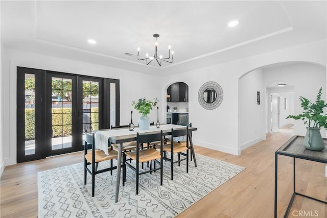 dining room featuring baseboards, arched walkways, light wood-type flooring, and a raised ceiling